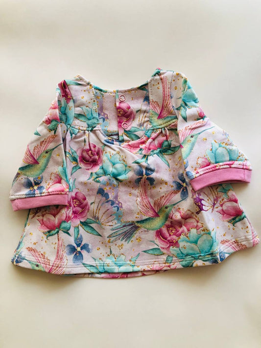 Kleitiņa “Kolibri un ziedi” 50–52 — viegli siltināts cilpiņtrikotāža, spiedpogas pie kakliņa, garās piedurknes